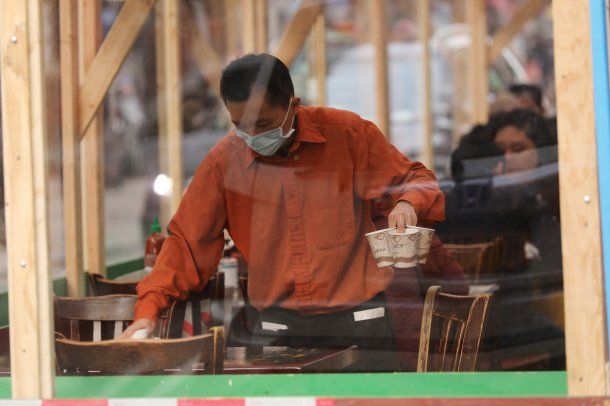 Un mesero con barbijo levanta vasos de café descartables de un bar en Estados Unidos